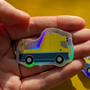 A pale white palm sits across the image holding a 5cm holographic sticker of Dublin Bus's Buspidéal rescue truck